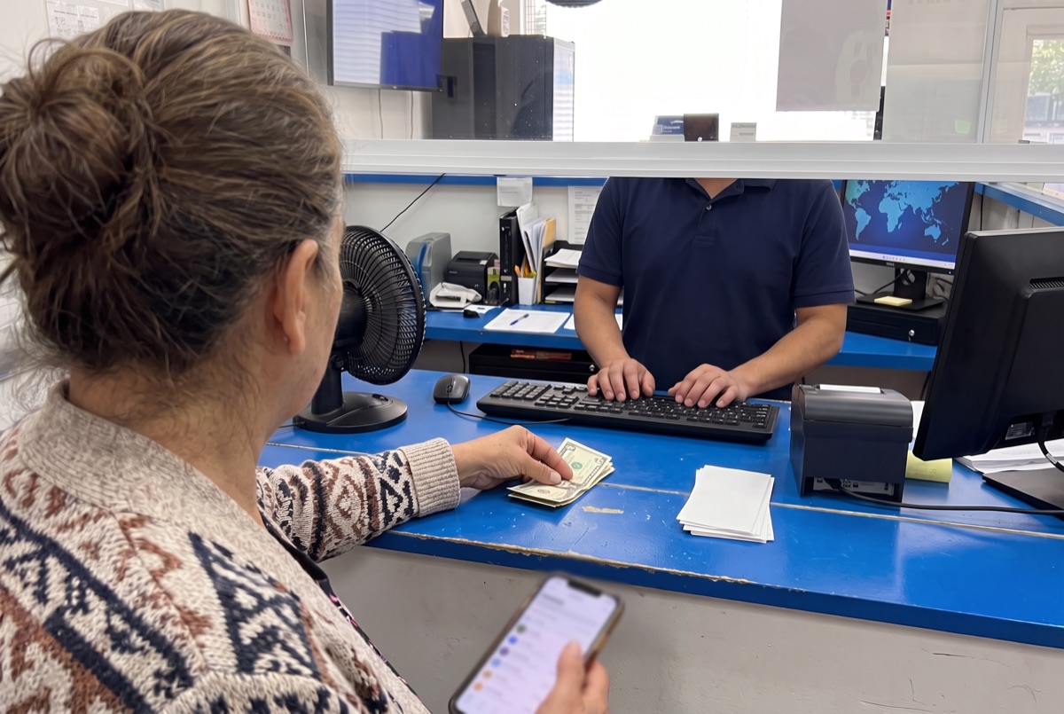 Una señora entrega el dinero en el mostrador mientras le registran el envío en la computadora